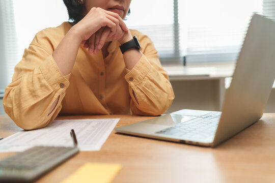 Worried Asian woman sitting at a desk with laptop, calculator and financial documents, representing financial stress, household expenses, bills and personal finance planning.