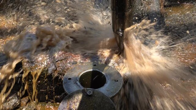 Close up of long metal bailer pipe extracting crude oil with splash at Wonocolo traditional oil well, Bojonegoro, East Java, Indonesia. Traditional petroleum extraction and heritage mining process.