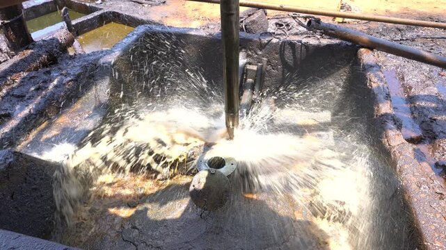 Close up of long metal bailer pipe extracting crude oil with splash at Wonocolo traditional oil well, Bojonegoro, East Java, Indonesia. Traditional petroleum extraction and heritage mining process.
