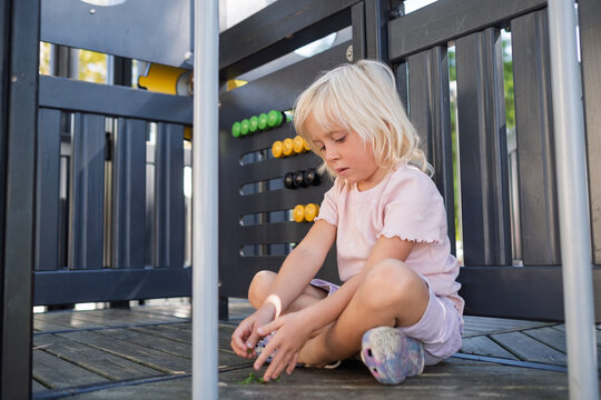  little girl sitting on wooden floor playing alone at outdoor playground