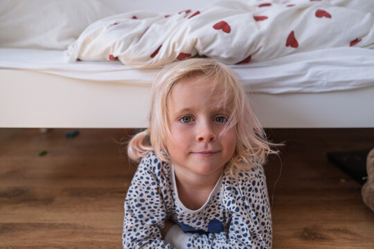  blonde little girl in pajamas lying on wooden floor in cozy bedroom
