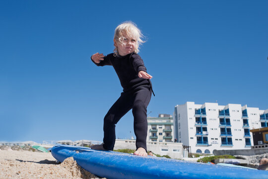  girl in black wetsuit practicing surf balance on board at sandy beach