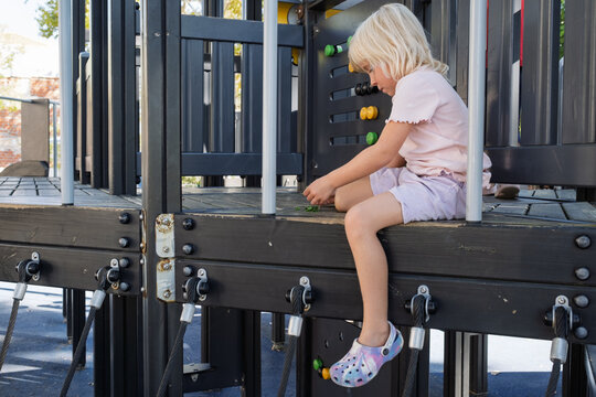  little girl sitting on wooden floor playing alone at outdoor playground