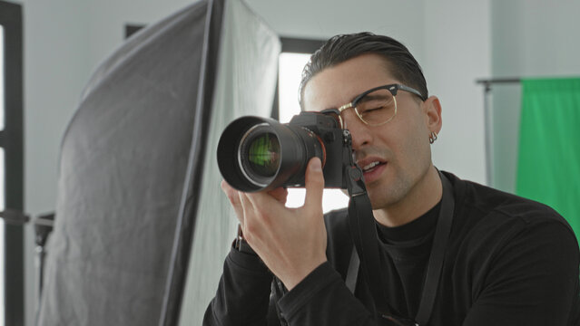 Man holds camera and points finger while directing a studio session with softbox and green screen visible; instructional focus.