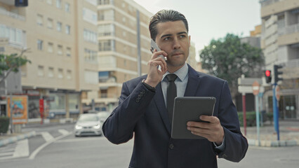 Man talking on smartphone while holding tablet on a city street, checking screen and notes  focused efficiency. © Krakenimages.com