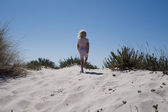 little girl walking up white sandy dune with coastal vegetation under blue sky