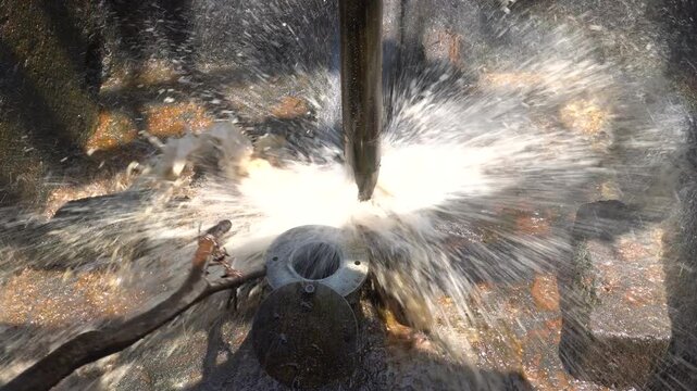 Close up of long metal bailer pipe extracting crude oil with splash at Wonocolo traditional oil well, Bojonegoro, East Java, Indonesia. Traditional petroleum extraction and heritage mining process.