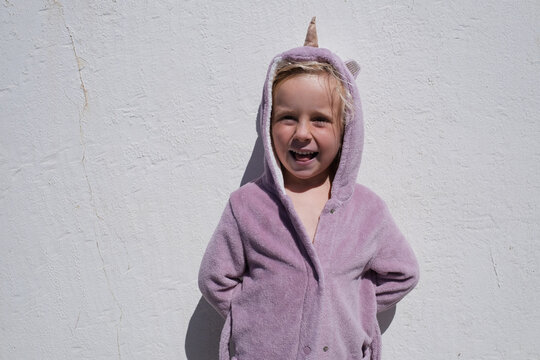 little girl wearing funny unicorn hooded bathrobe against white textured wall