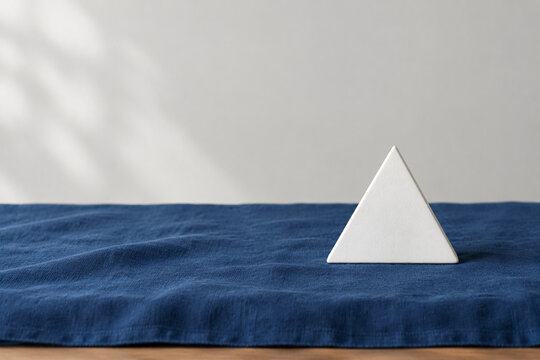 Single white equilateral triangle object on deep blue linen, calm still life for editorial concept