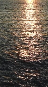 Sunset casts vibrant orange and yellow colors over the ocean, with boats gently bobbing on the water's surface, creating a serene evening atmosphere
