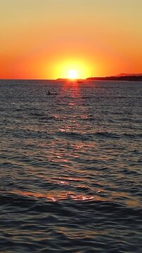 Sunset casts vibrant orange and yellow colors over the ocean, with boats gently bobbing on the water's surface, creating a serene evening atmosphere