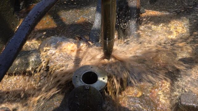 Traditional oil well extraction process in Wonocolo, Bojonegoro. Long steel pipe dipping into petroleum well hole, splashing liquid around concrete pit during manual crude mining in Indonesia.