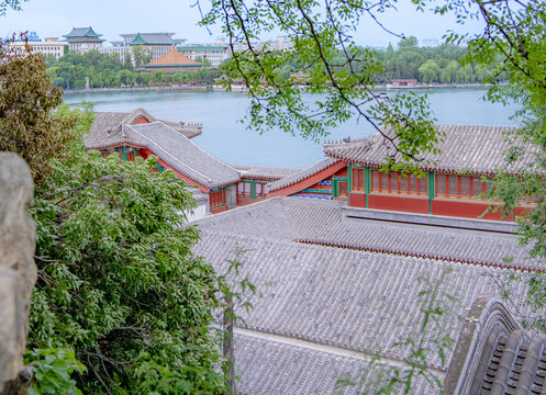Traditional Chinese pavilion roofs overlooking lake with distant pagoda and city skyline