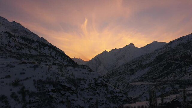 4K Landscape shot of snowy Himalayan mountain range with orange clouds above them during the sunset in winter season as seen from Keylong in Lahual and Spiti district, Himachal Pradesh, India.