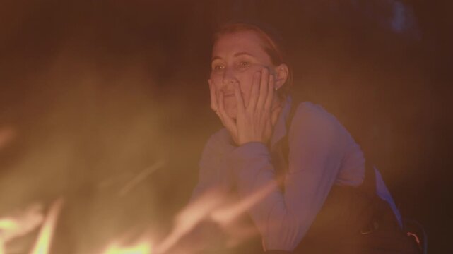Young woman sits in front of the bonfire burning in the wild
