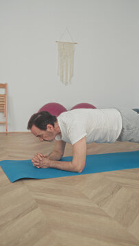 Man holding forearm plank on blue yoga mat in studio with exercise ball and parquet floor visible; mindful focus.