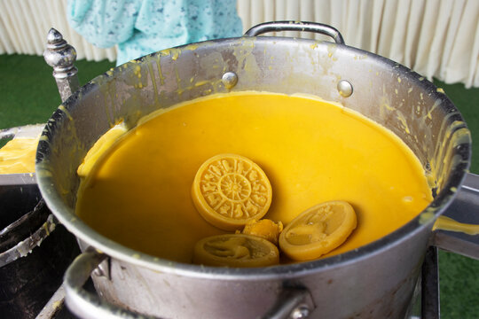 Closeup merit ritual rite thai cultural tradition people join of boiling yellow wax sheets melting in hot liquid wax pot for casting Buddhist Lent candles at Wat Tha Luang temple in Phichit, Thailand
