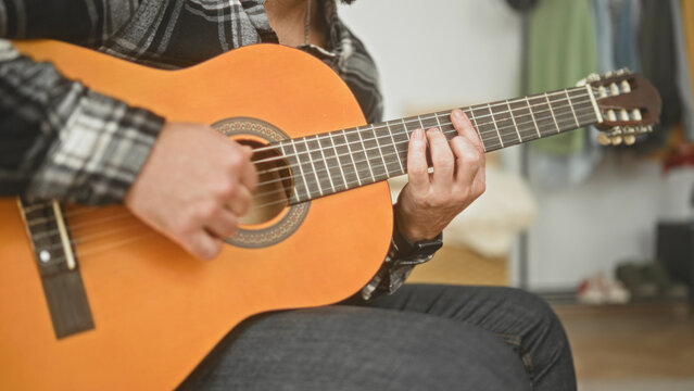 Man playing a classical guitar, fingers on the fretboard and right bare hand strumming chords while seated in a studio; calm concentration.