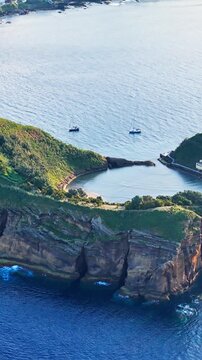 Scenic volcanic ring with inner lagoon and rocky perimeter rising from Atlantic ocean waves near Sao Miguel, aerial view