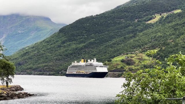 Distant cruise ship moving along Norwegian fjord against coastal mountains