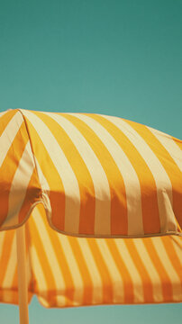 yellow and white striped beach umbrella against turquoise background, minimalist summer vacation photography with copy space for travel advertising, poster or seasonal design