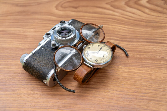 Vintage film camera with old eyeglasses and antique wristwatch on wooden table. Nostalgic retro accessories in close-up composition.