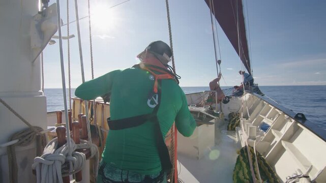 Crew work with the sails on the big expeditional sailing vessel moving in the Atlantic Ocean