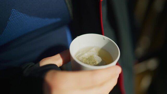 Close-up of hands holding a white cup with a steeping tea bag. The warm herbal drink provides comfort in cold weather.