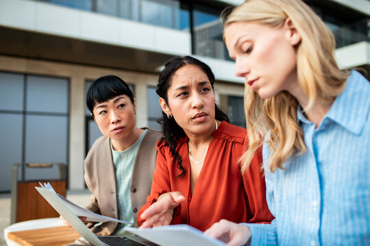 Three businesswomen reviewing documents on an outdoor office terrace