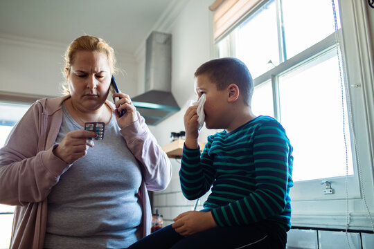Concerned mother calling doctor for sick son in home kitchen
