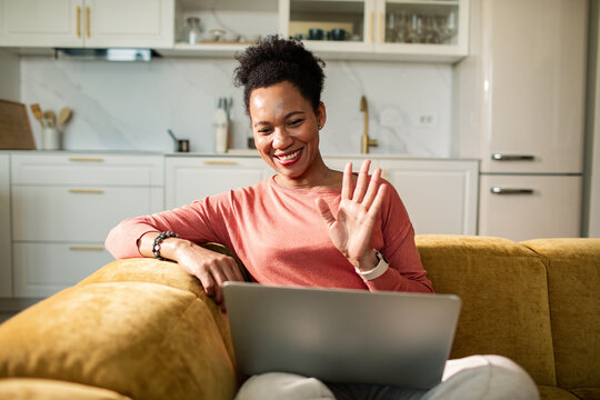 Smiling woman waving during video call on sofa at home