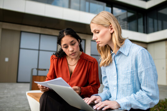 Two colleagues reviewing documents on laptop outside office