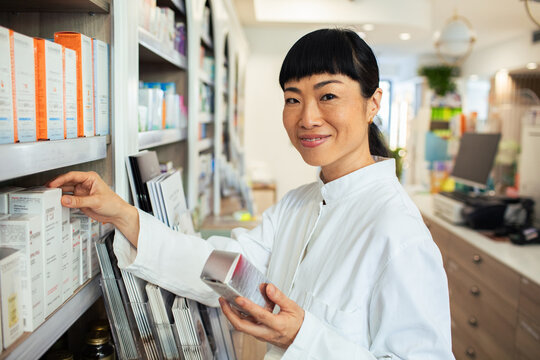 Smiling female pharmacist stocking medicine on shelves in modern pharmacy