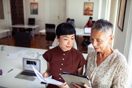 Two businesswomen collaborating with tablet in modern coworking office