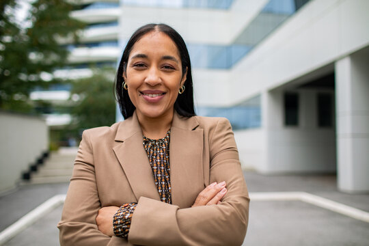 Confident businesswoman smiling with arms crossed outside modern office building