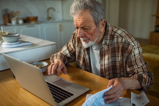 Senior man paying bills online at home kitchen table
