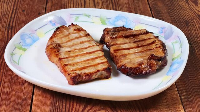 Serving of grilled pork steaks on plate on rustic table