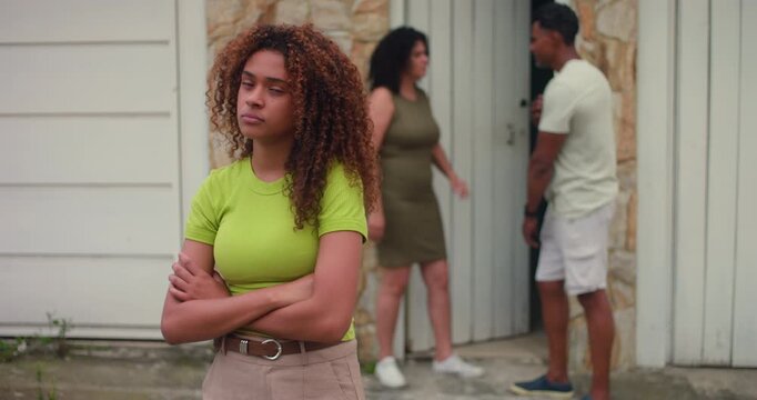 Teenage girl standing with arms crossed, looking frustrated and upset, parents arguing in background, family conflict, emotional strain, feeling unheard and overwhelmed