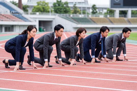 陸上トラックのスタート地点に並ぶ若手ビジネスマンとビジネスウーマン