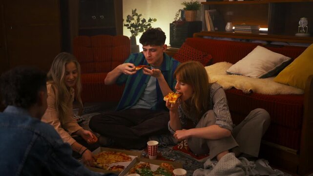Young happy people eating pizza and laughing together at home party