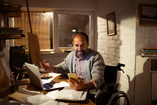 Wheelchair user on smartphone at home office desk