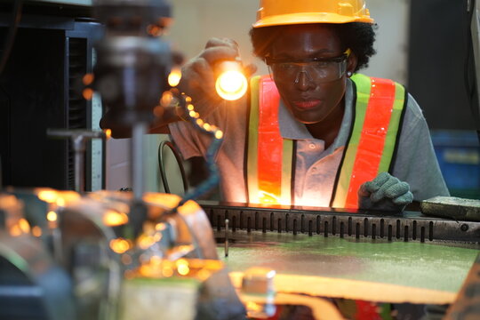 Female industrial worker inspecting CNC machining process with flashlight in manufacturing factory