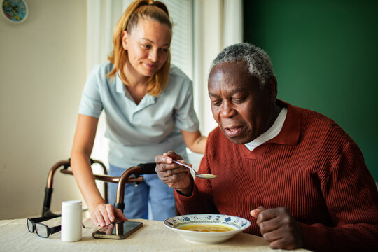 Caregiver helping senior man eat soup at home