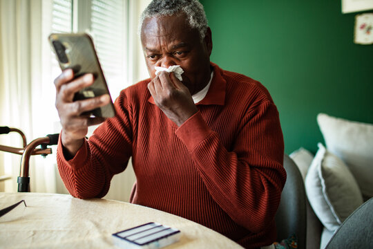 Older man blowing nose during telehealth call at home