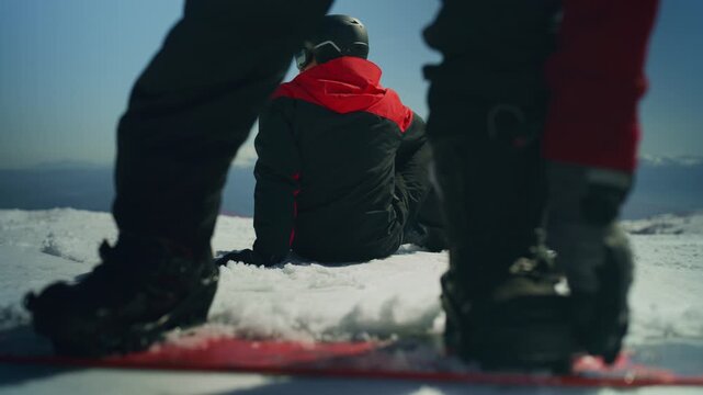 Two friends pause their snowboarding adventure on a pristine snowy mountain, one seated while the other stands. They are enjoying a moment of rest and the spectacular winter mountain scenery.