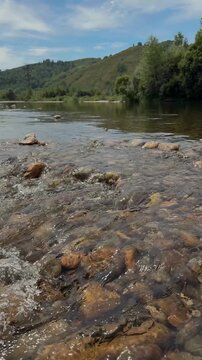 Shallow River Flowing Over Rocks Below Green Hills in Daylight