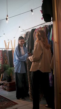 Casual Women Sharing Style Insights In Store. Two Women Fashion Shopping Amidst Plants And Vintage Finds