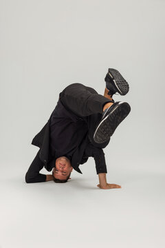 Male breakdancer performing an upside down freeze pose in black sportswear, isolated on a light grey studio background. Athletic b-boy showcasing strength, balance, and street dance agility.