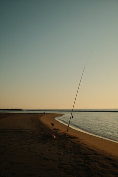 Silhouette of a fisherman casting a rod from a beach at sunset