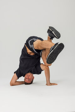 Dynamic breakdancer performing an upside-down freeze stance in studio. Athletic young b-boy balancing on head and arms against a plain background wearing black sportswear.